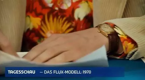 Man in 70s attire at a news desk with vintage computers, introducing the Flux model.