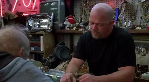 Gollum-like character with pale skin and large eyes in a grey hoodie holds a gold ring at a pawn shop counter.