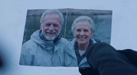 Elderly man with oxygen mask and ice axe climbing a snowy mountain, looking at a photo.