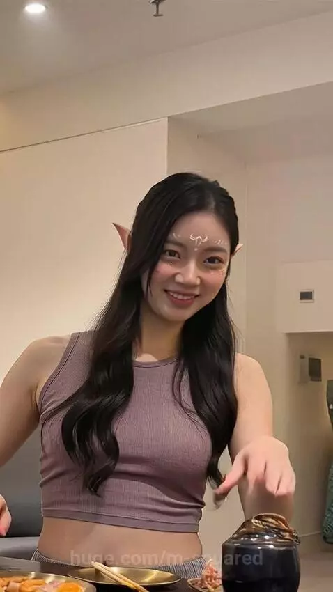 Woman with elf ears and face paint cooking a hotpot meal at a table with mushrooms and asparagus.