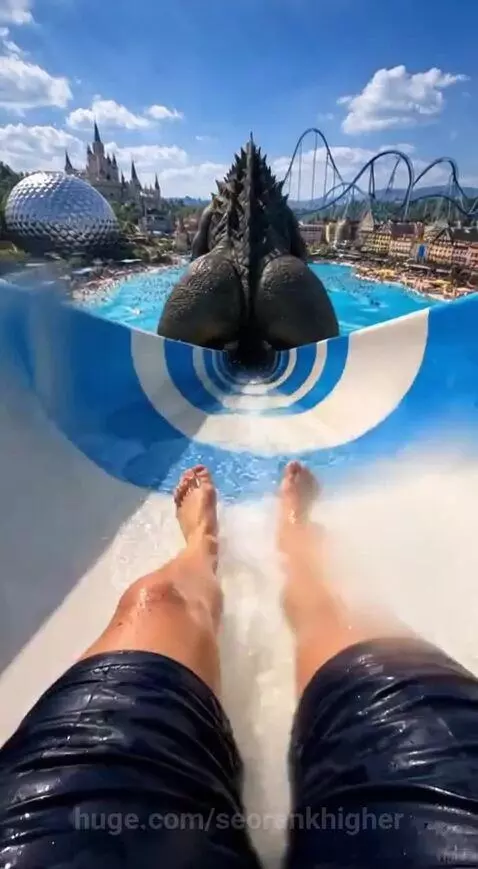 First-person view of a person riding a fast water slide at a vibrant amusement park.