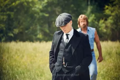 Chuck Norris smiling after punching a Tommy Shelby lookalike in a grassy field.