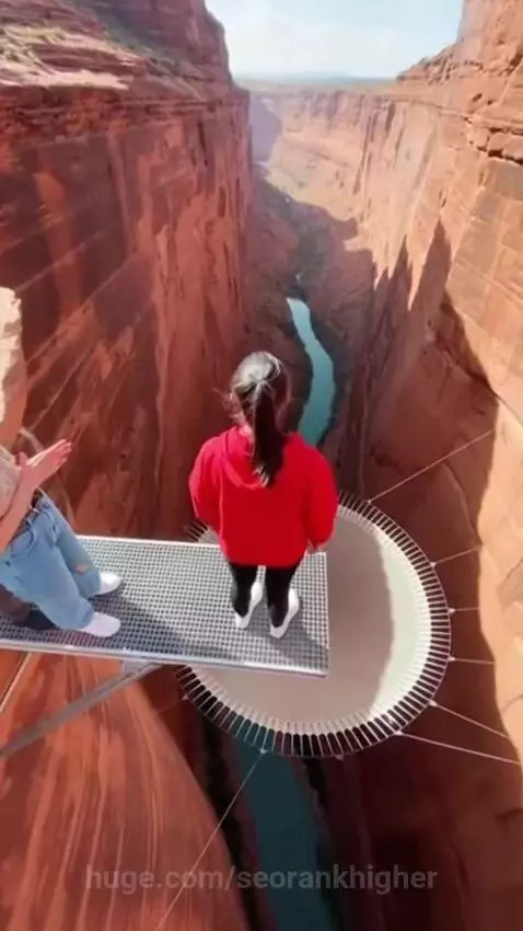 Person in red hoodie jumping across a canyon onto a large trampoline net.