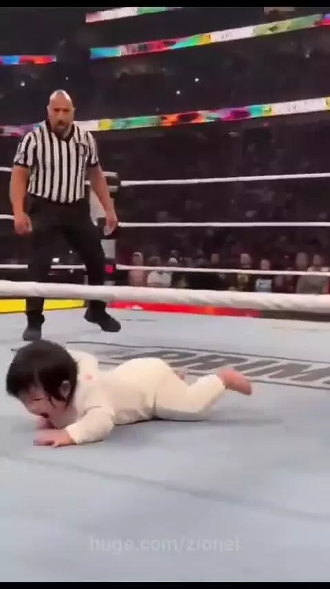 Baby in a wrestling ring performing a body slam on Dwayne 'The Rock' Johnson with a cheering crowd.