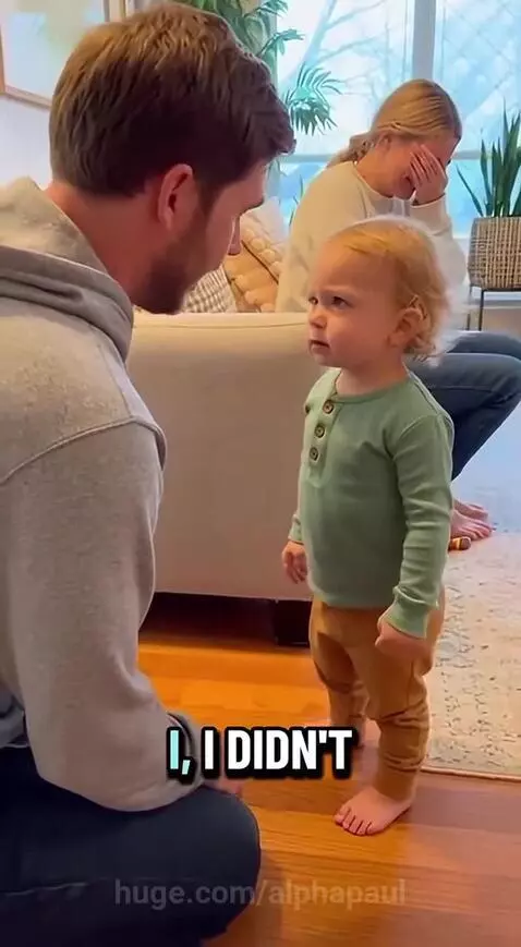 Toddler with serious expression tells dad 'Don't say sorry!' while mom laughs in background.