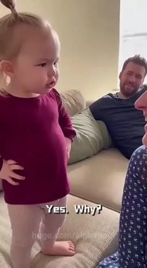 Young girl sternly tells an adult woman not to approach her dad, who is smiling in the background.