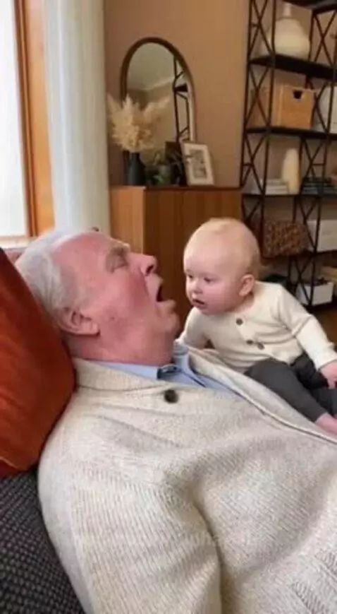Baby sitting next to a sleeping grandpa, mimicking his snoring sound and then laughing.