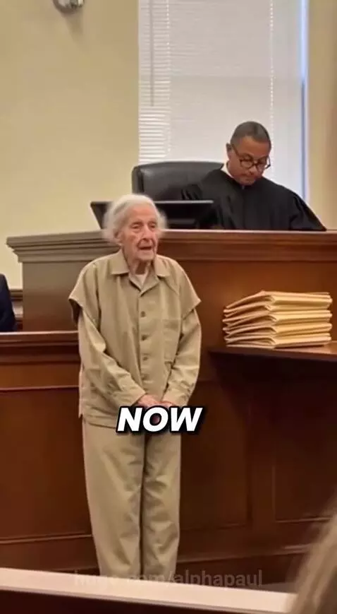 Elderly woman in prison uniform looking confused and sad in a courtroom after being told she is free to go.