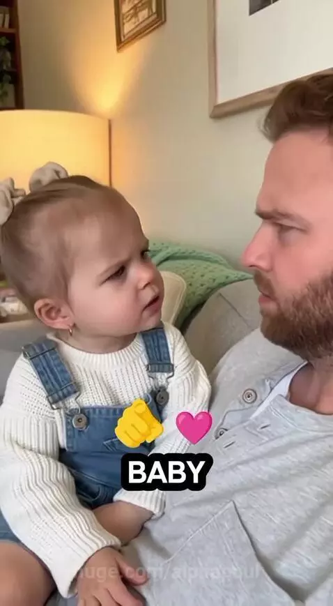Young child in overalls asks a bearded man on a couch if he is mommy's baby.