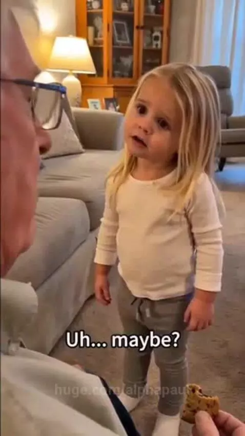 Young girl playfully pointing finger at her grandfather who is holding a cookie.