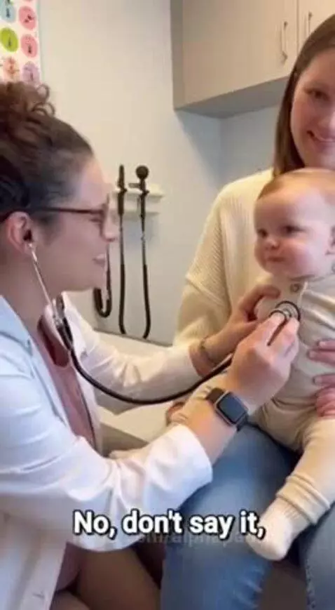Baby sitting on a woman's lap in a medical office, mimicking a doctor with a stethoscope.