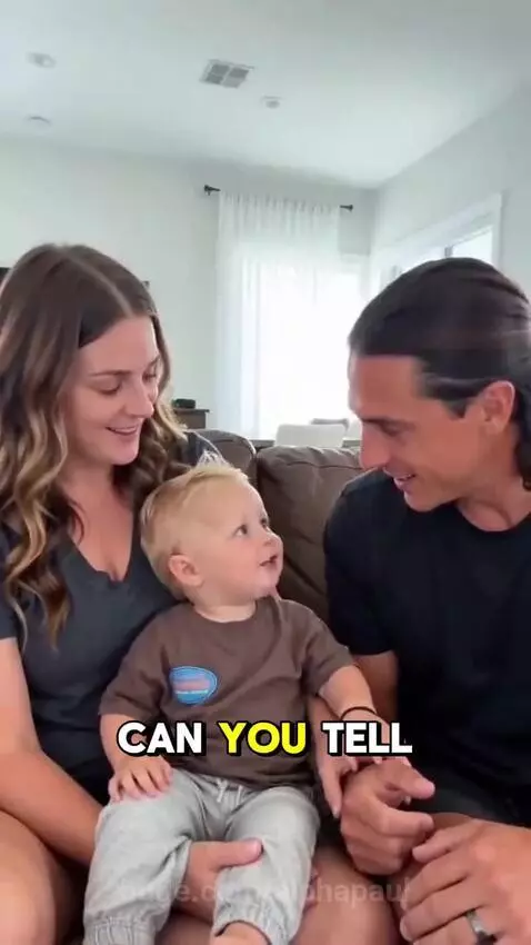 A smiling baby sits on a man's lap while a woman sits next to them, all in a living room.