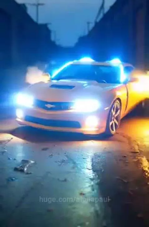 Yellow Chevrolet Camaro transforming into the robot Bumblebee with blue and orange lights and smoke.