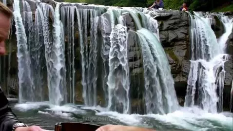 Two men play cards at a table with a majestic multi-tiered waterfall cascading in the background.