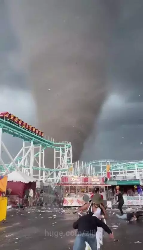 Tornado approaching an amusement park, people running in panic, swing ride being tossed by wind.