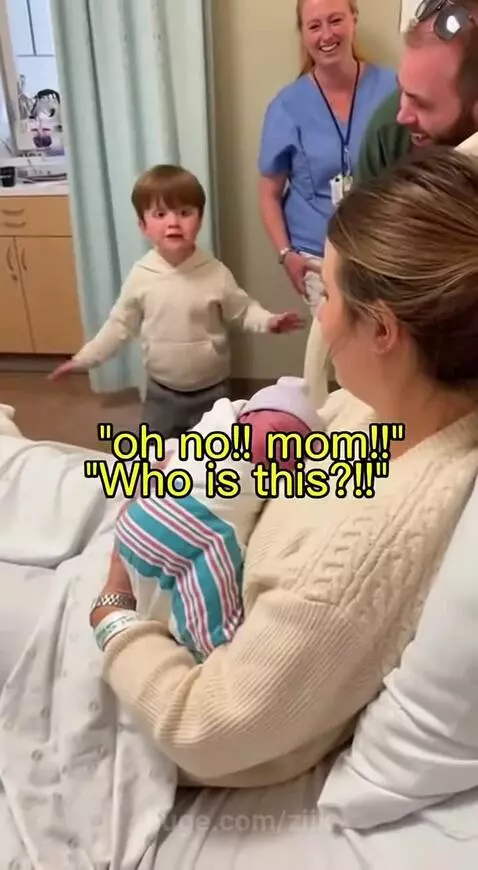 Young boy looking shocked while standing next to his mother holding a newborn baby.