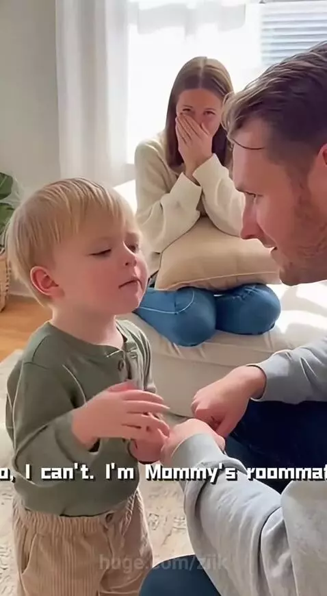 A young boy stands talking to a kneeling man, while a woman laughs in the background.