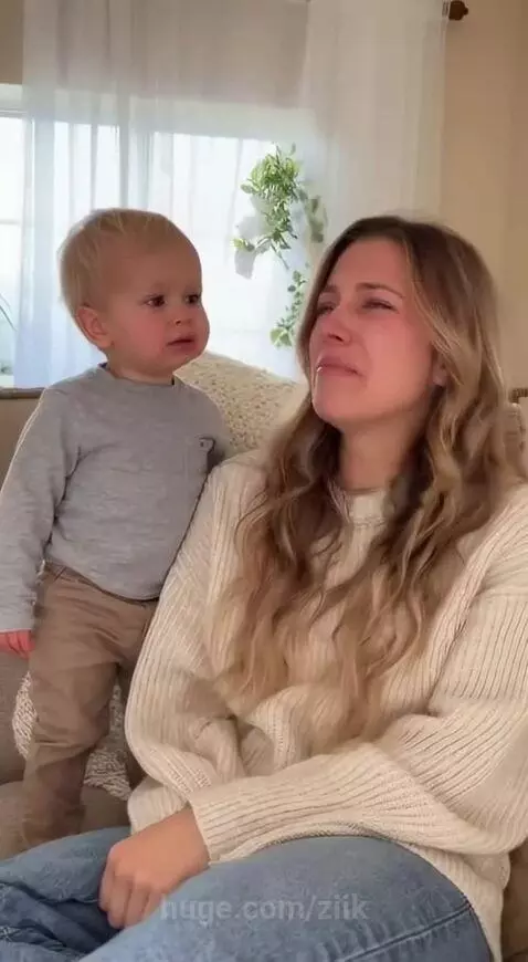 A young blonde woman crying on a couch as a toddler boy stands beside her, looking concerned.