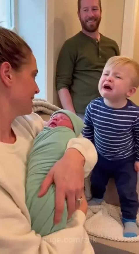 A toddler cries and asks for kisses while a mother holds a newborn baby.