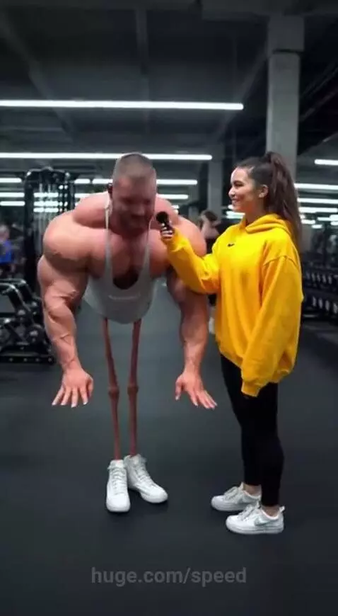 Muscular man with extremely thin, elongated legs struggling to do a push-up in a gym, while a woman laughs.