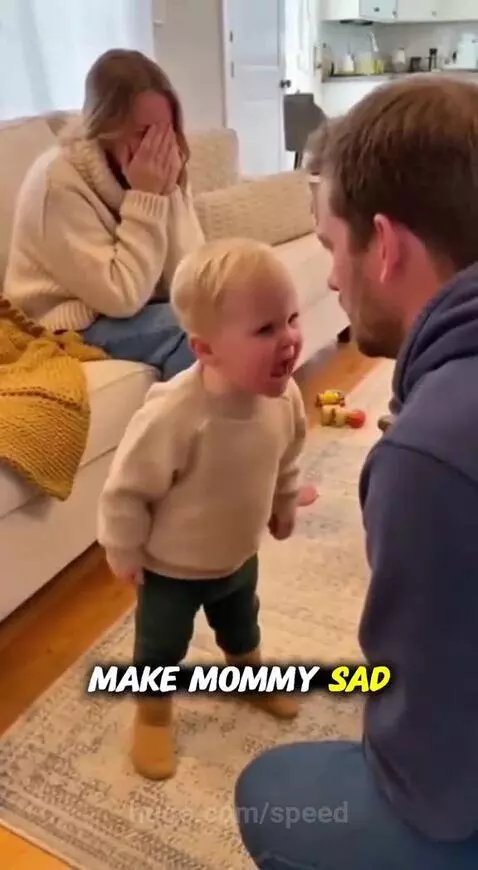 Toddler in sweater and boots sternly points finger at dad, demanding he apologize to mom.
