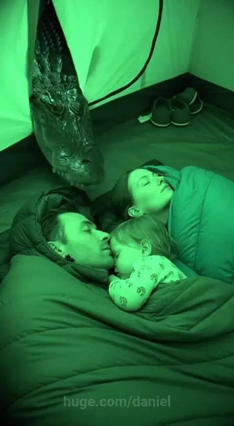 A realistic alligator head lunges into a green-lit tent where a family is sleeping.