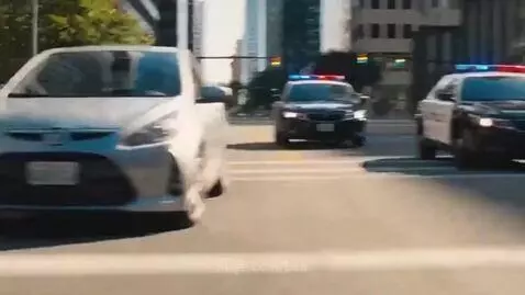 Two monkeys in a car, one driving, being chased by a police car through a city street.