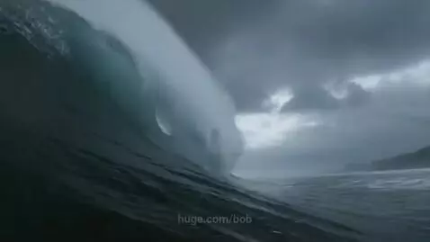 Massive ocean wave curling and breaking from a low perspective, with stormy, overcast skies.