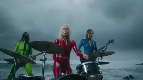 Three women in latex outfits performing as a rock band on a rocky shore during a lightning storm.
