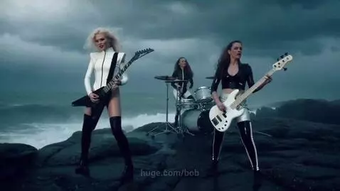 Three women performing metal music on a dark, rocky shore during a stormy night with lightning.