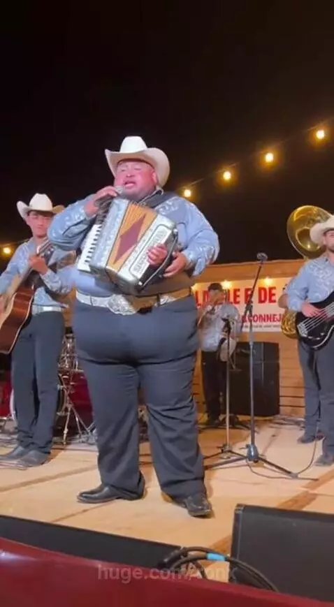 A man in a cowboy hat falls through a collapsed stage floor during an outdoor band performance at night.