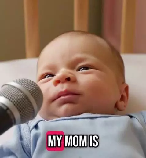 Close-up of a baby in a crib with a microphone near its face, looking unimpressed.