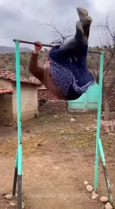 Elderly woman in traditional attire falls from a horizontal bar but smiles and laughs after landing.