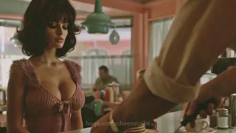 Woman with dark hair and pink top at a diner counter, ordering pancakes from a chef.