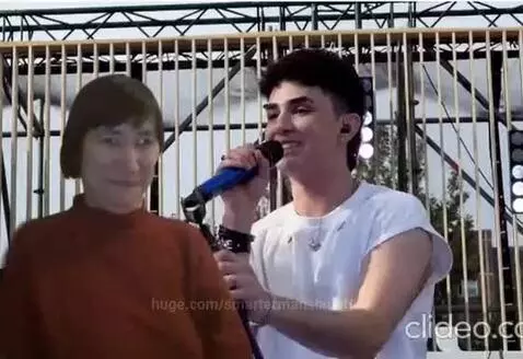 Male singer in white shirt and female in turtleneck embrace and kiss on stage during a performance.