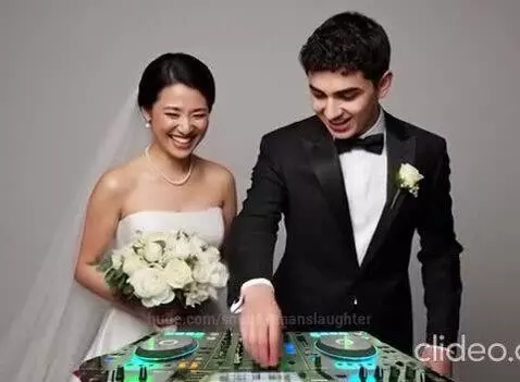 Bride in white gown and groom in tuxedo smiling behind a DJ mixer with green and blue lights.