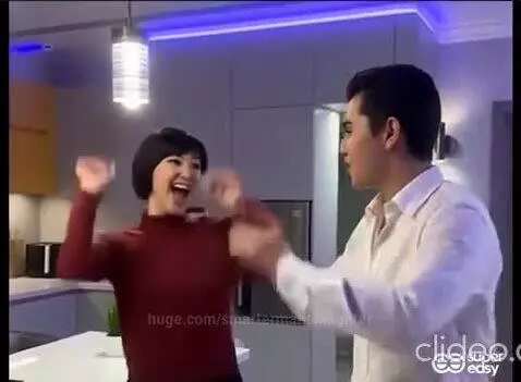 Couple dancing and smiling in a kitchen with blue LED lights, woman in red, man in white shirt.