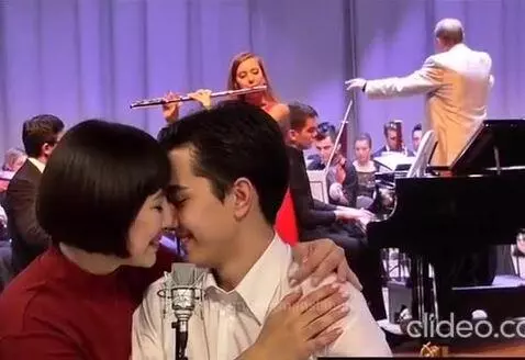 Couple kissing in front of a microphone with a live orchestra performing in the background.