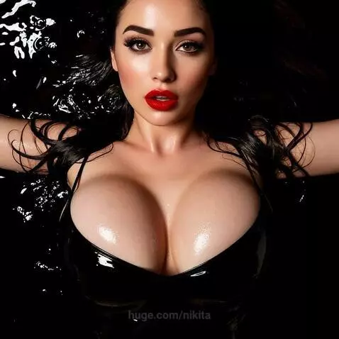 Overhead view of a woman with dark hair and red lipstick submerged in dark water, wearing a shiny black top.