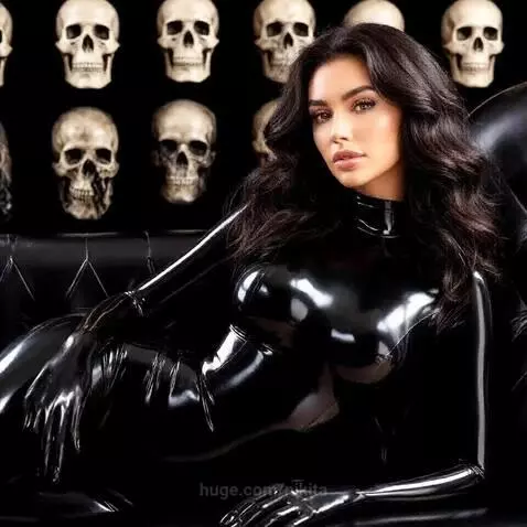 Woman in a full-body shiny black latex suit lying on a black leather couch, with skulls in the background and blue lighting.