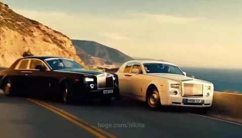 Two Rolls-Royce Phantom cars, one black and one white, in a high-speed chase on a winding coastal road.