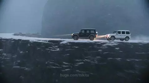 Two Mercedes G-Wagens driving on a narrow, rickety bridge over a chasm in a snowy mountain landscape.