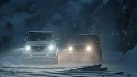 Two Mercedes-Benz G-Wagons driving at high speed on a snowy mountain road with a stormy backdrop.