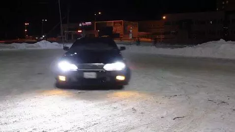 Dark Toyota Chaser JZX100 crashes into a metal streetlight pole during a snowy drift at night.
