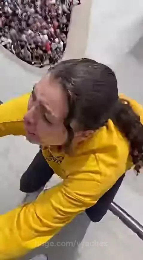 Person on a scooter falling down a large concrete skate ramp, with spectators watching.