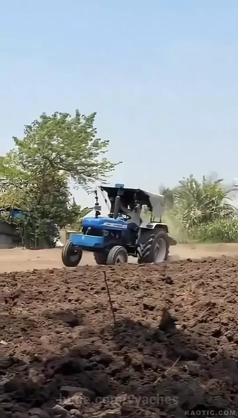 A blue New Holland tractor plowing a dusty field with a man operating it.