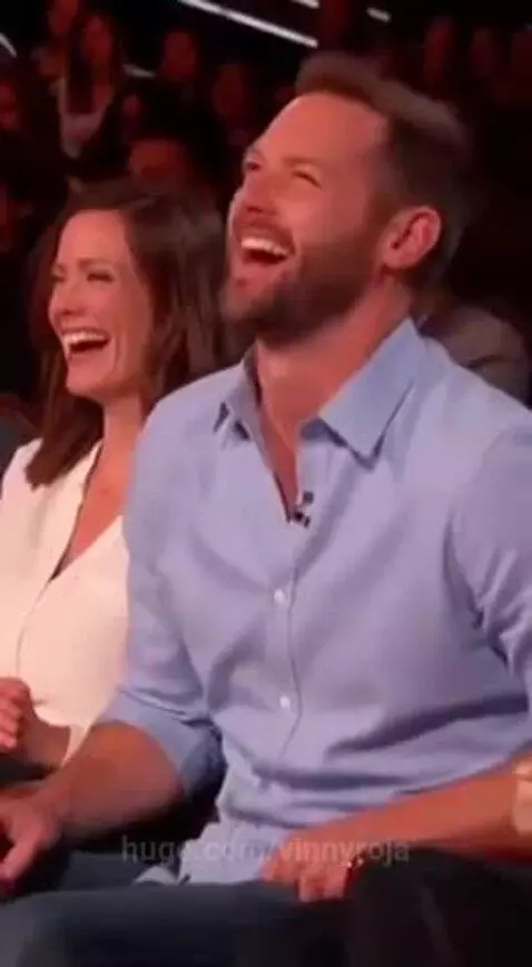 A young girl speaking into a microphone, with adults laughing in the background.