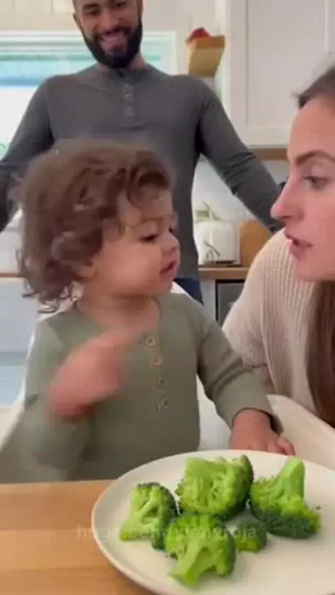 Toddler with curly hair sitting at a table, refusing to eat broccoli, calling it a tree.