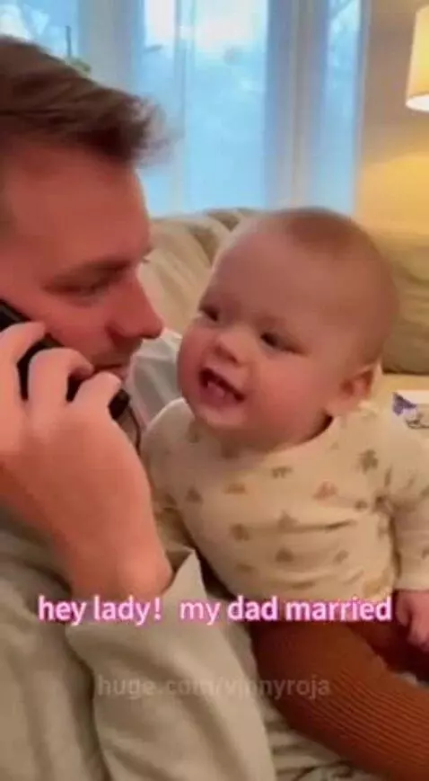 Baby sitting on a man's lap, looking serious while the man talks on the phone.