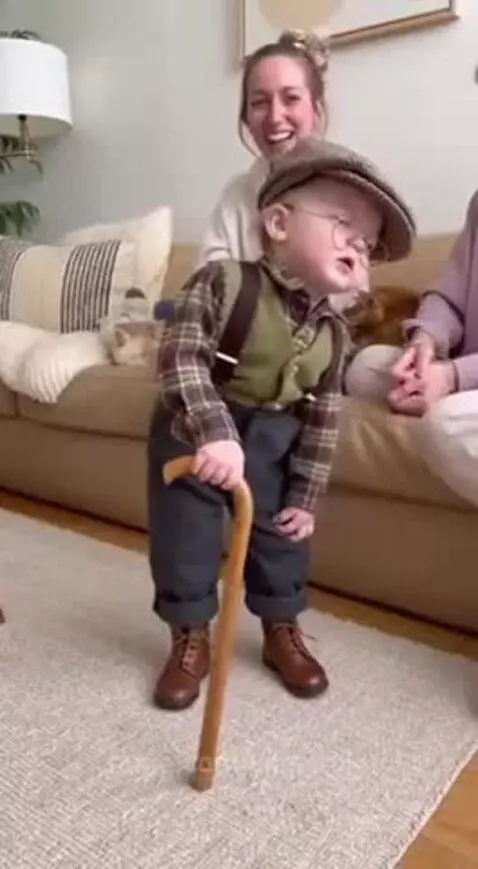 Baby dressed as an old man, wearing glasses, vest, and holding a cane.